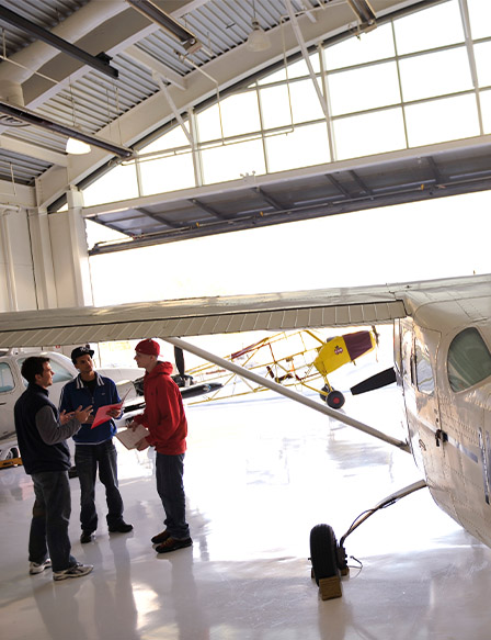 3 students talking by plane in hangar